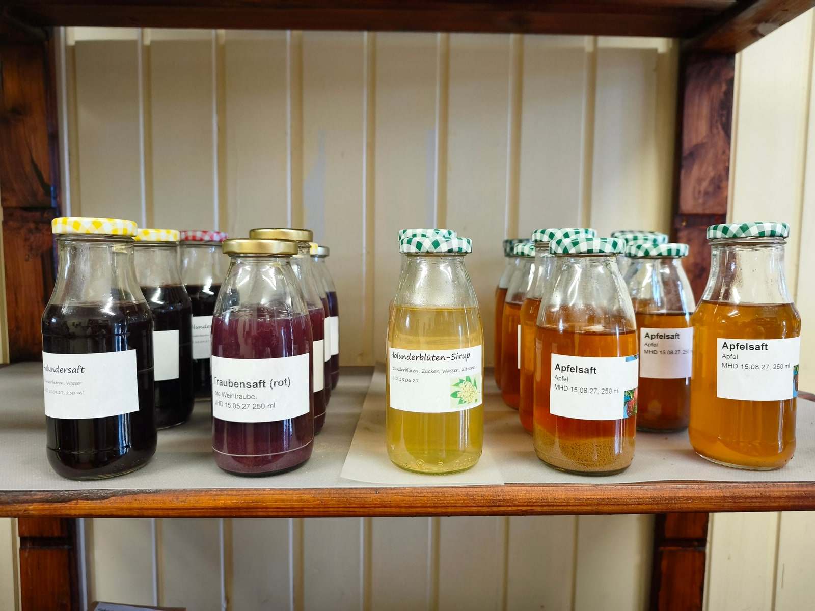 Sieben Saftflaschen stehen in einer Reihe auf einem Brett im Verkaufswagen, von fast schwarzem Holundersaft über roten Traubensaft und hellen Holunderblütensirup bis zu goldgelbem Apfelsaft.